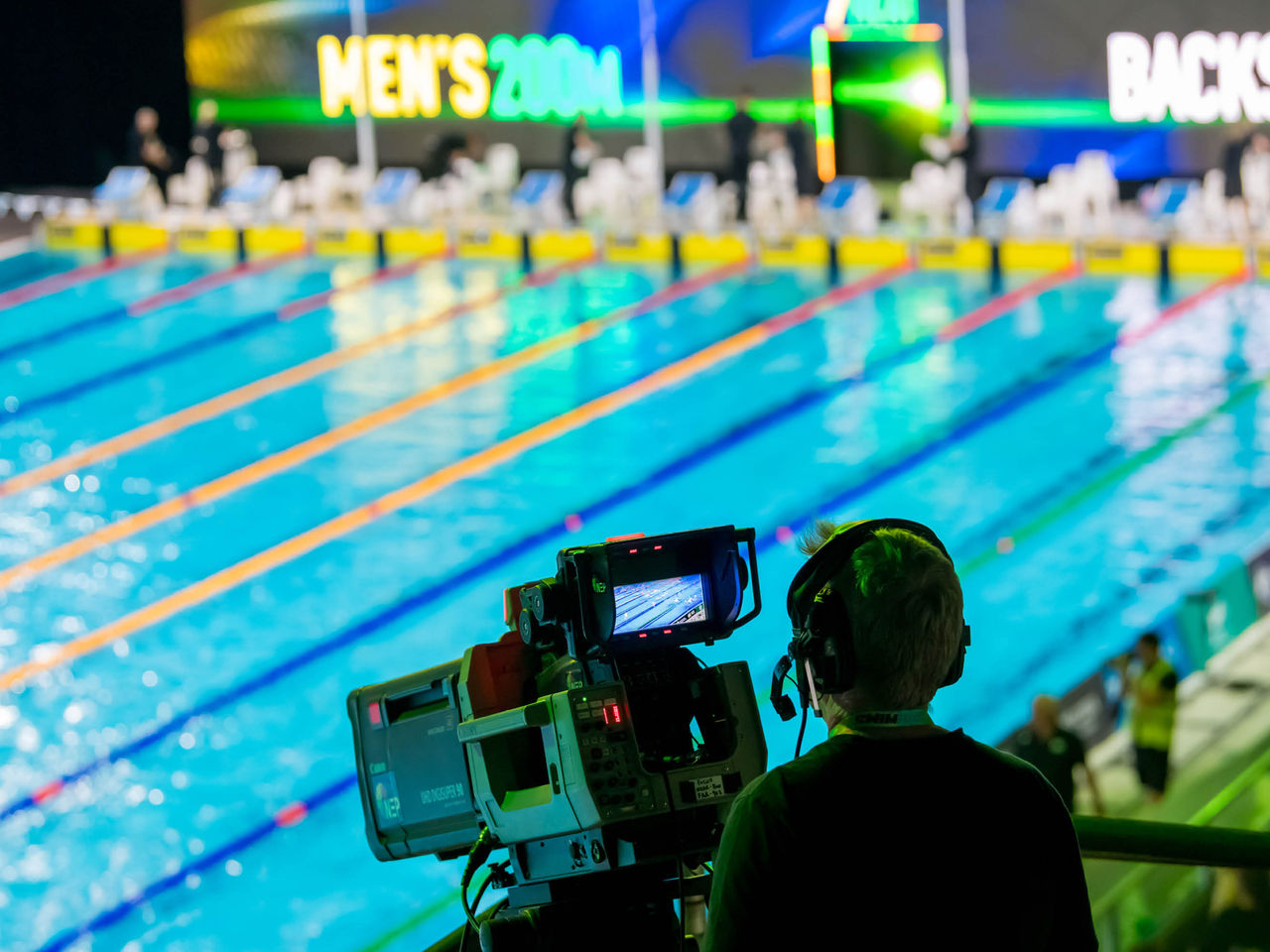 Video camera with person standing behind, swimming pool in the background